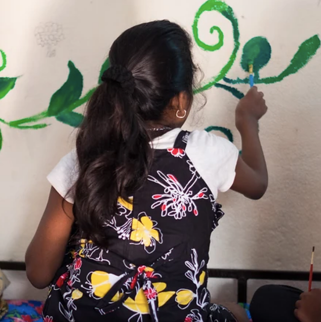 India girl, survivor of human trafficking or gender abuse painting a mural wall at shelter in India