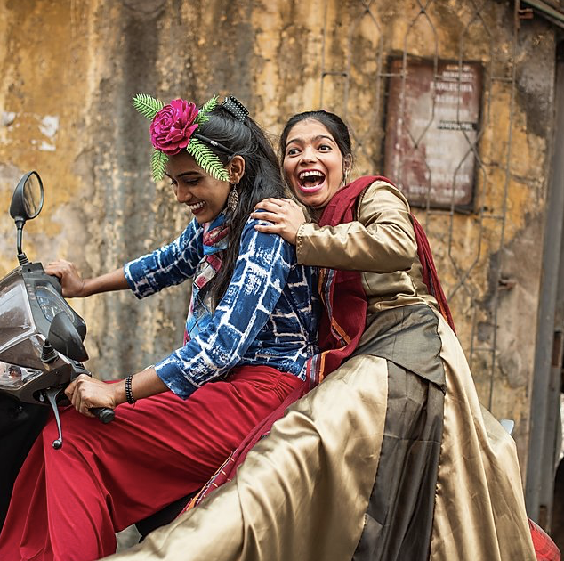 India women in colorful saris laughing on scooter in Kolkata, India